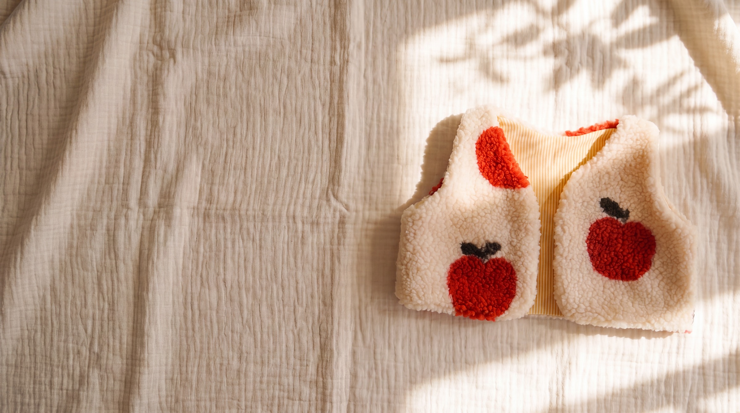 Handgenähte Weste aus cremefarbenem Teddyfleece mit Apfelmuster, flach auf hellem Musselin